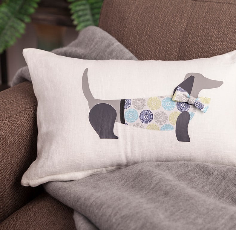 A custom pillow decorated with an iron-on vinyl puppy sits on a couch.
