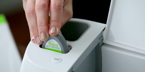 A triangle-shaped Cricut cartridge is inserted in a Explore Air.