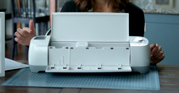 A woman points to the cartridge slot on a Cricut Explore.