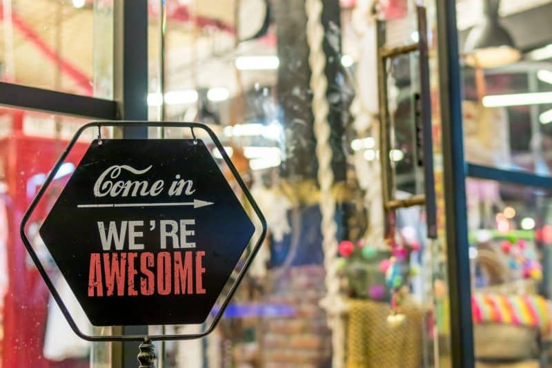 A sign in front of a colorful store reads: Come in, we're awesome