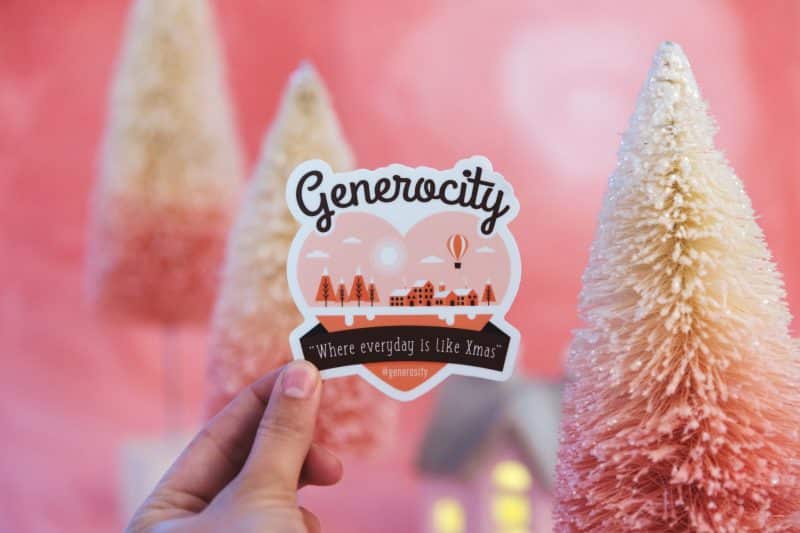 A hand holds a DIY vinyl sticker in front of a pink Christmas wonderland