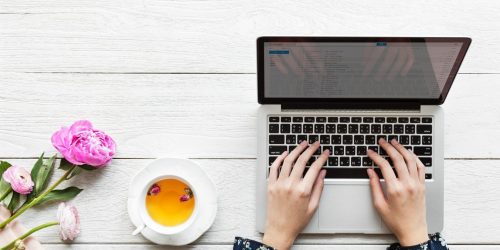 A woman types at her laptop with tea and flowers