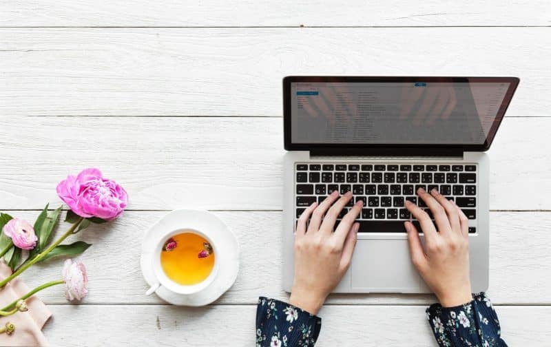 A woman works at her laptop with tea and flowers