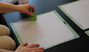 A woman uses a green plastic scraper to to clean a cutting mat.