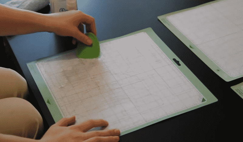 A woman uses a green plastic scraper to to clean a cutting mat.