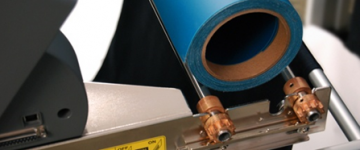 A roll of blue specialty material is being fed into a professional cutter.
